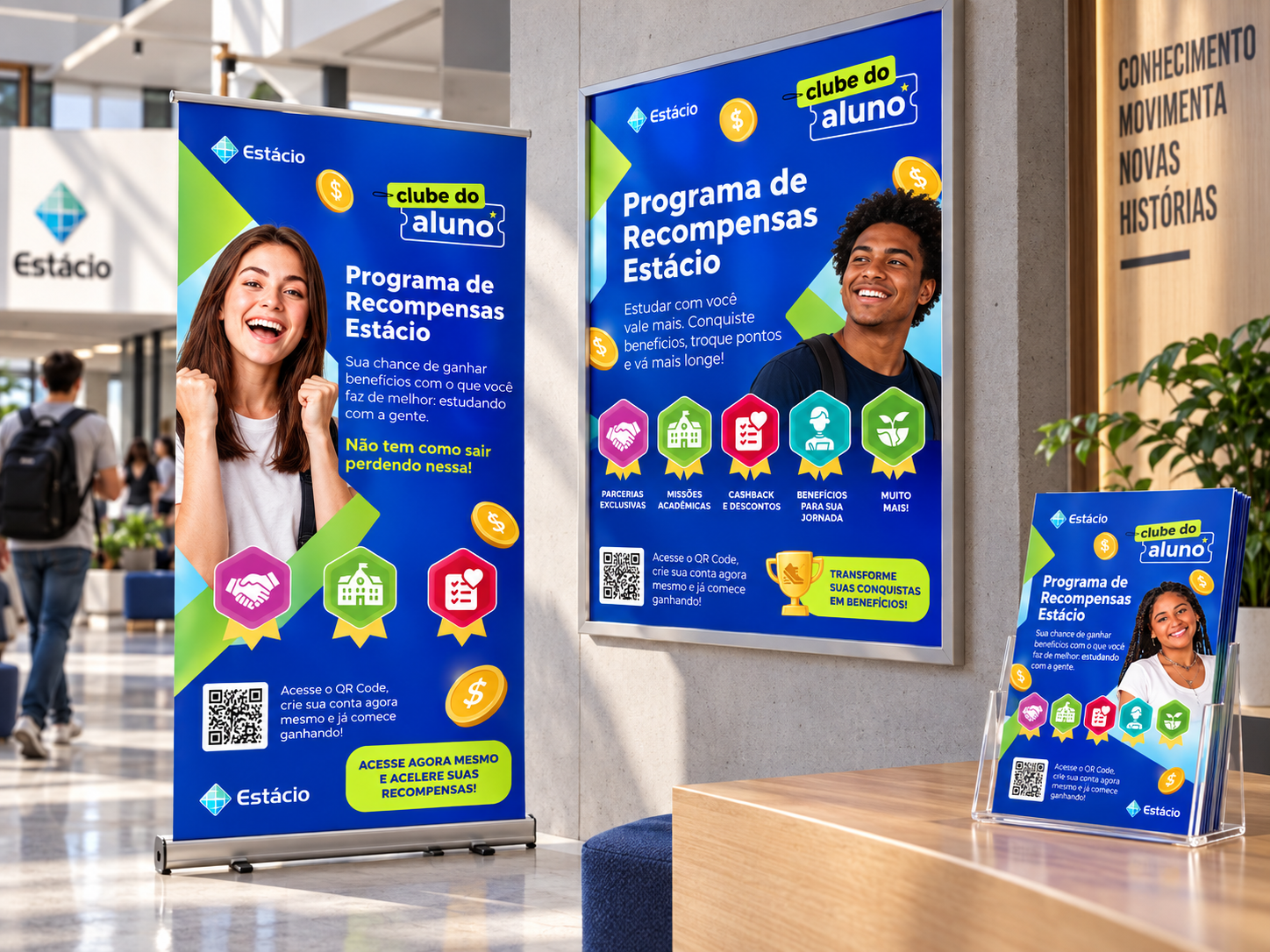 Roll-ups e painel promocional do programa instalados em espaço universitário, com medalhas e a identidade visual da campanha.