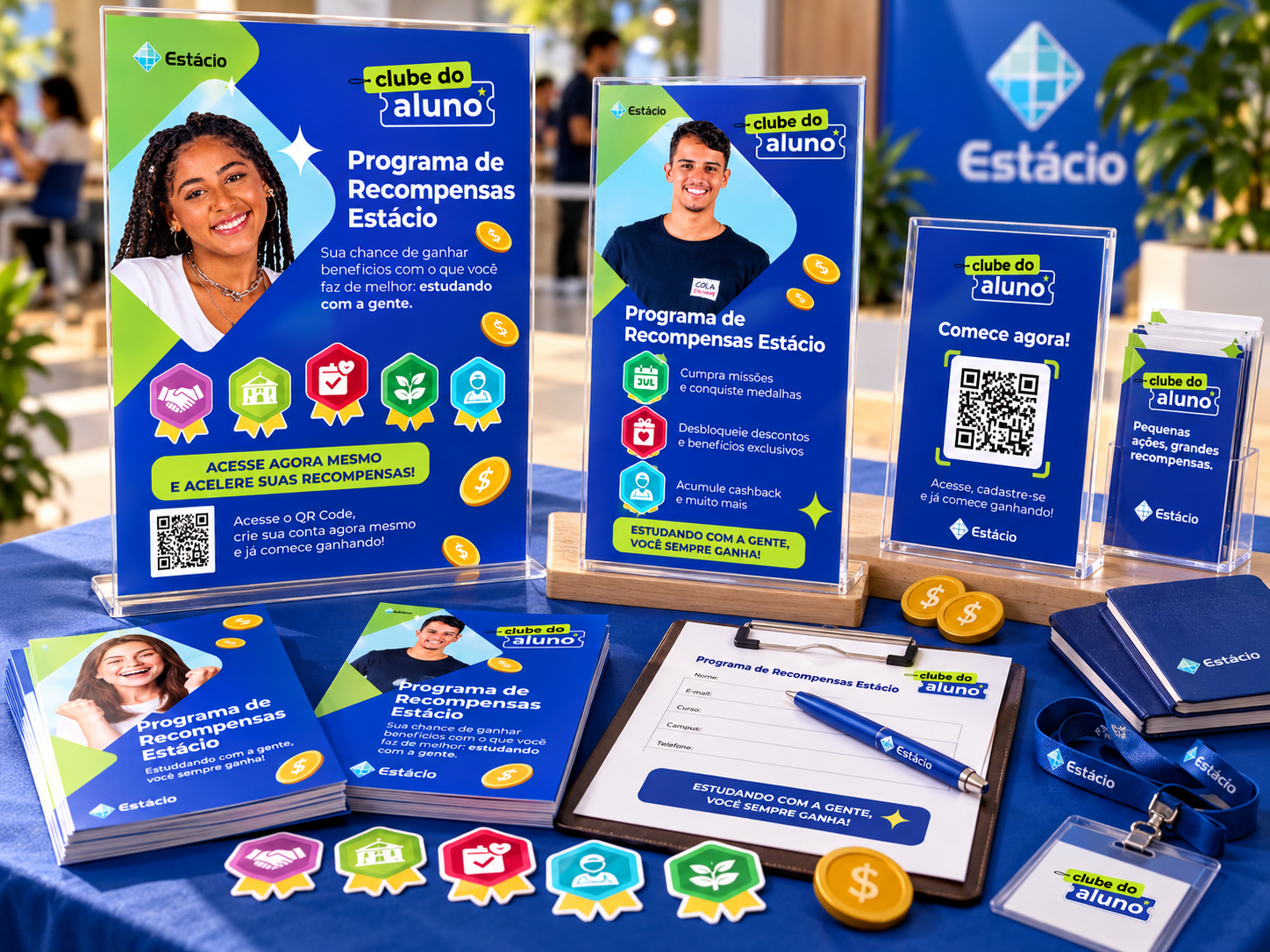 Mesa de materiais promocionais do programa, com sinalização, medalhas, brindes e peças gráficas em ambiente universitário.